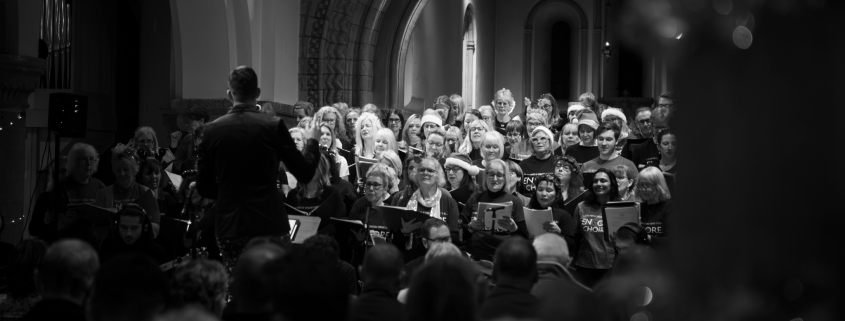 Choir performing during a Christmas concert inside a church with a conductor leading the singers.